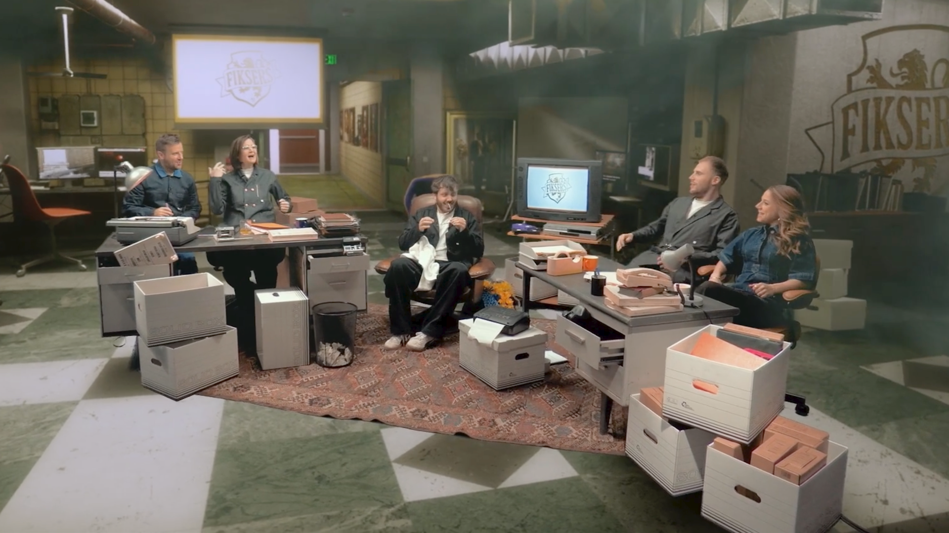 Fikser cast sitting in a vintage office set with FIKSER logo on screen